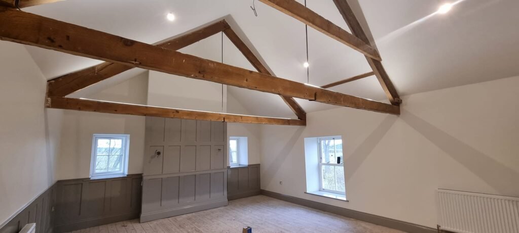 Vaulted room with exposed beams and sage panelling, decorated by North & Sons